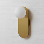Three-quarter front view of this Clérachic brass wall light, the white globe overlapping the top of the rounded plate.