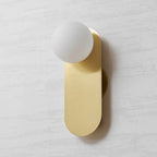 Brass wall light from Clérachic with a frosted white globe, photographed slightly from the right on a textured wall.