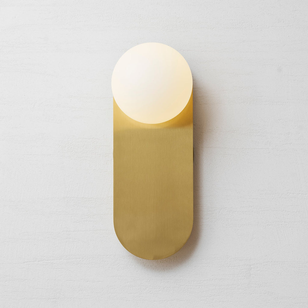 Straight-on view of the brass plate and white globe of this Clérachic wall light, with a soft shadow on the pale wall.