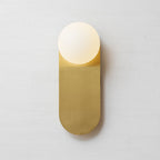 Straight-on view of the brass plate and white globe of this Clérachic wall light, with a soft shadow on the pale wall.