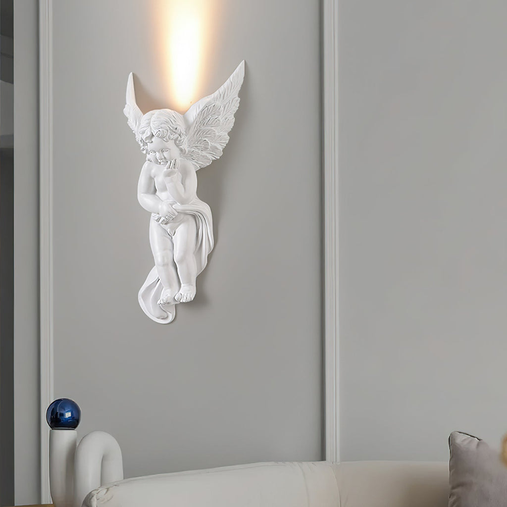 The cherub version of this Clérachic wall light, lit, sending a column of warm light up a grey panelled wall above a cream sofa.