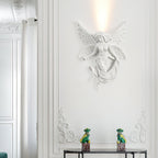 Lit fairy-shaped Clérachic wall light on a white moulded wall, with two small green figurines on a dark console below.