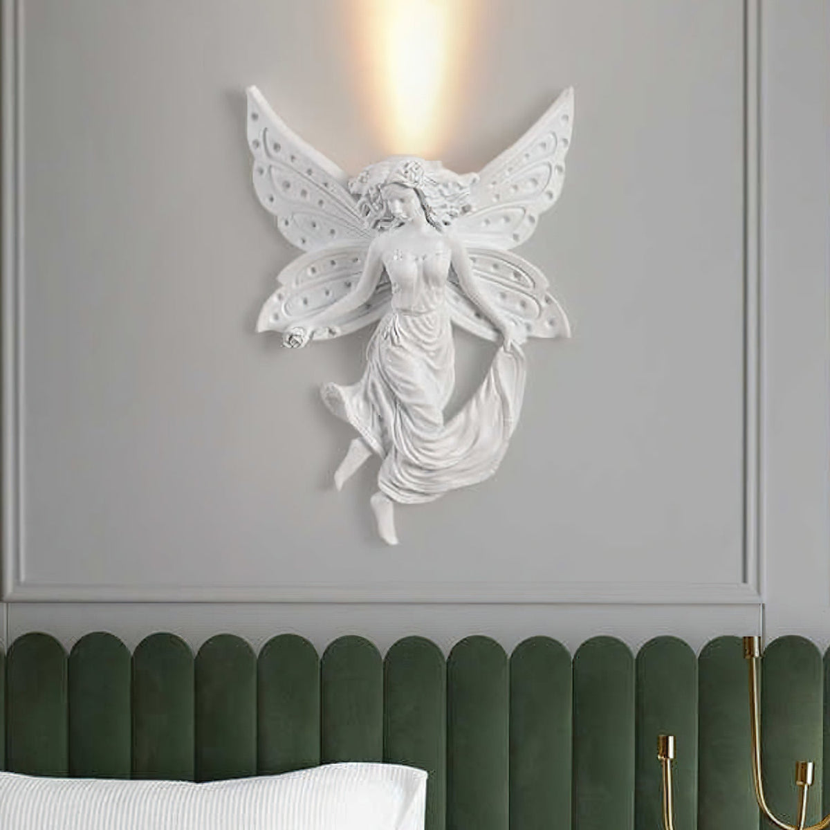 A Clérachic fairy wall light with perforated butterfly wings, lit, on a grey panelled wall above a green padded headboard.
