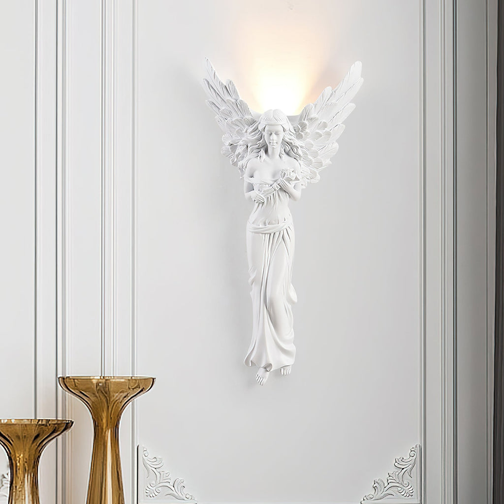 Standing-angel Clérachic wall light glowing on a white panelled wall, with two amber glass vases at the lower left.