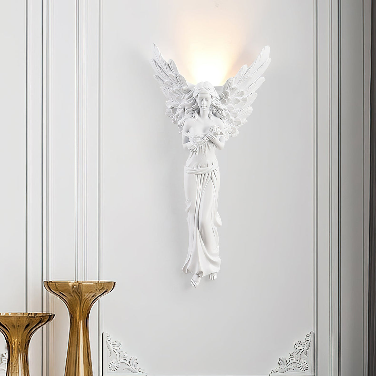 Standing-angel Clérachic wall light glowing on a white panelled wall, with two amber glass vases at the lower left.