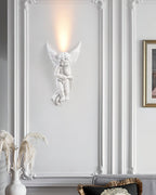 Cherub Clérachic wall light lit on a white moulded wall, with a vase of dried pampas grass at the lower left.