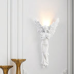 Standing-angel Clérachic wall light lit on a white panelled wall, with two amber glass vases standing in front of it.