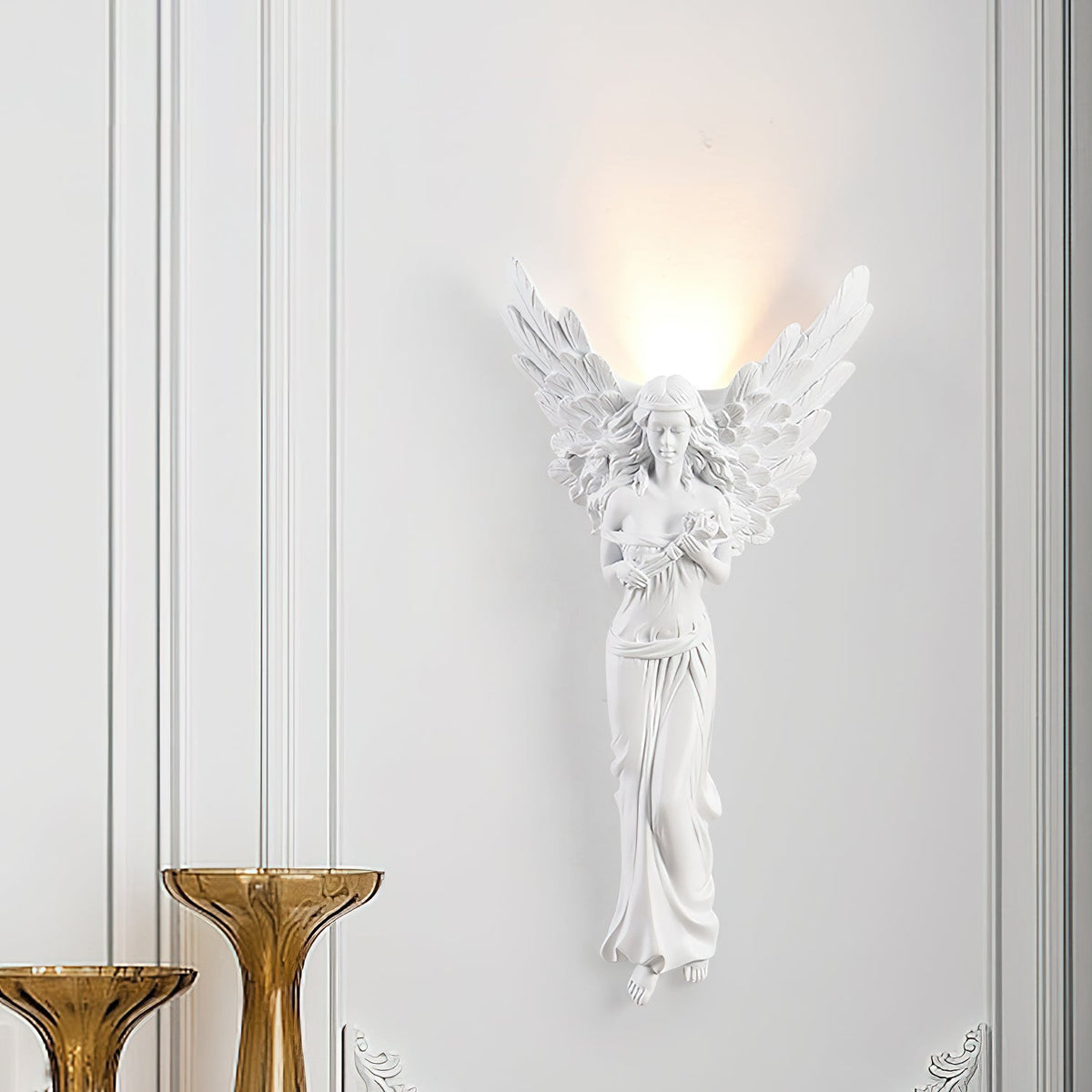 Standing-angel Clérachic wall light lit on a white panelled wall, with two amber glass vases standing in front of it.