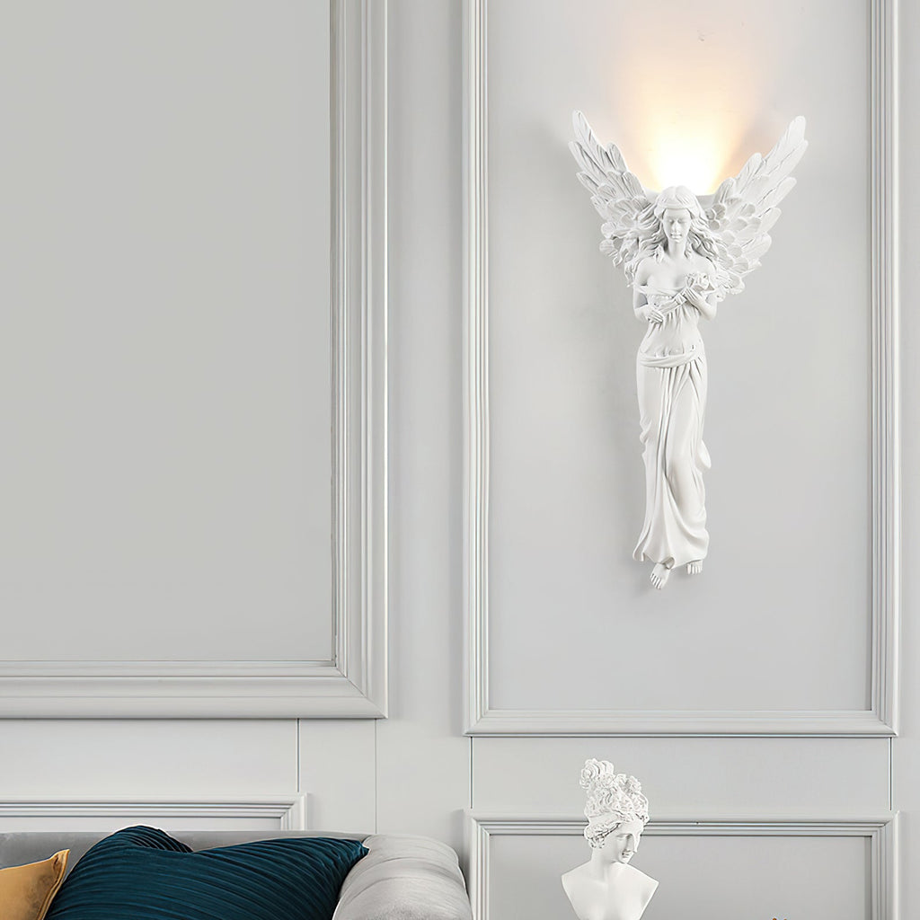 Standing-angel Clérachic wall light lit on a white panelled wall above a white bust and a teal cushion.