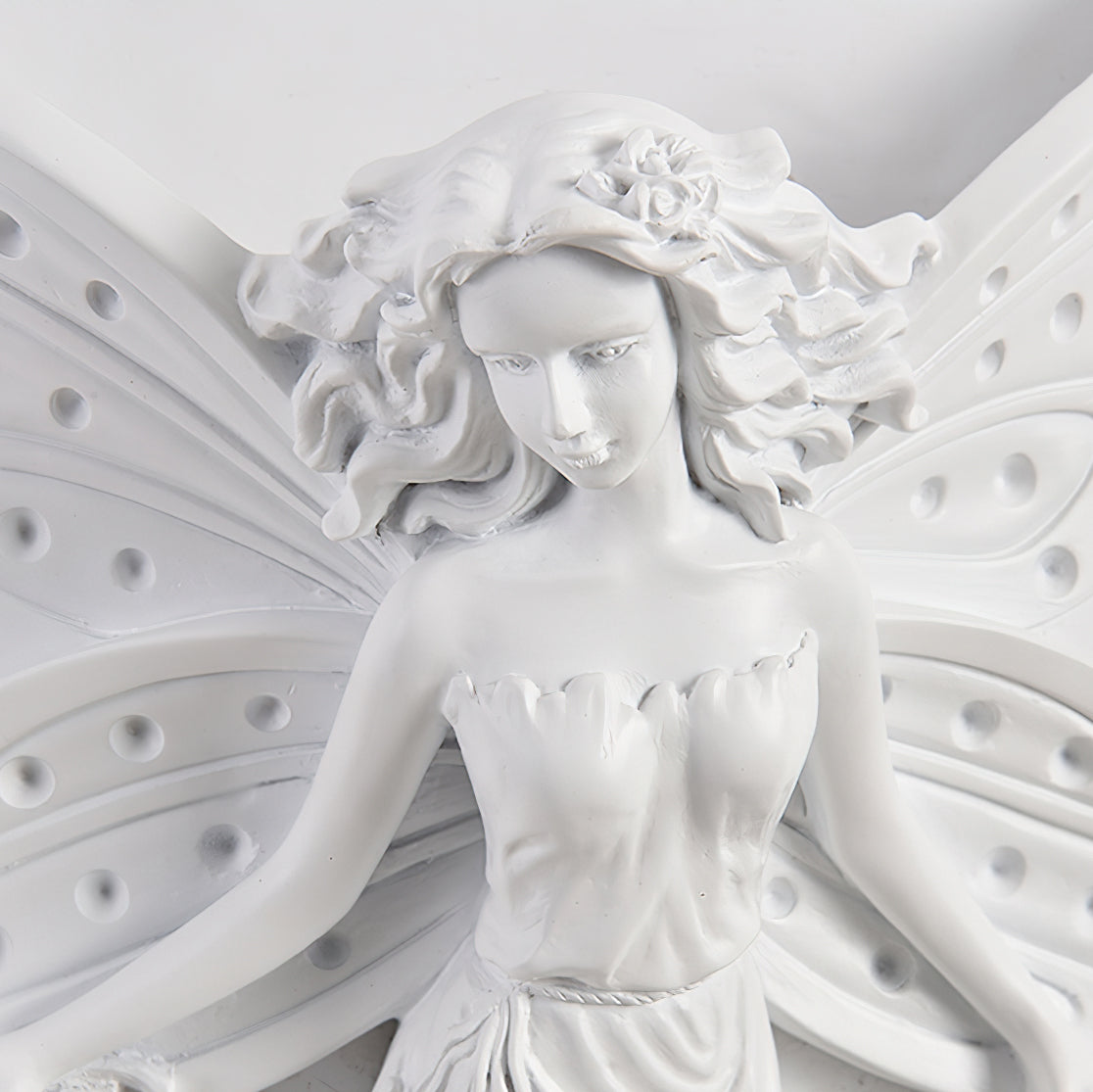 Close view of the fairy's face, flowered hair and perforated wings on this Clérachic white resin wall light.