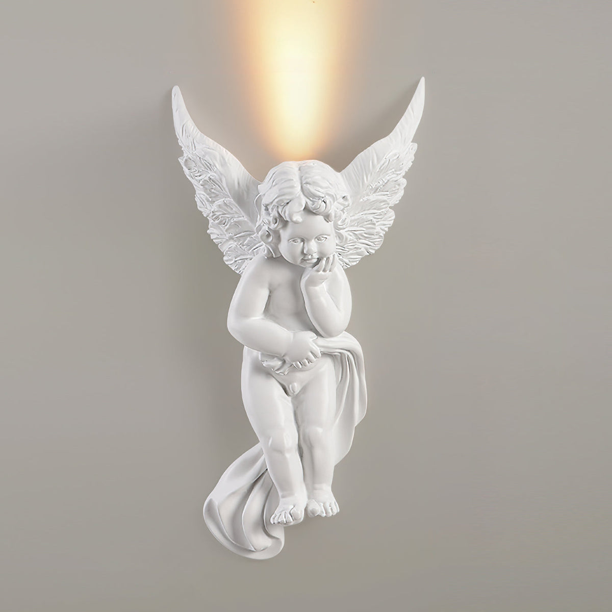 Cherub Clérachic wall light, lit, on a grey wall, a bright warm glow above its feathered wings.