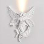Lit fairy-shaped Clérachic wall light on a pale wall, the warm uplight spreading above its perforated wings.