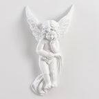 Unlit cherub Clérachic wall light on a pale wall, the figure resting its chin on its hand with cloth draped below.