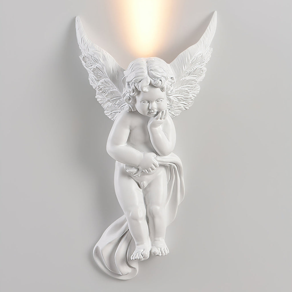 Lit cherub Clérachic wall light on a pale wall, with warm light rising from behind its feathered wings.
