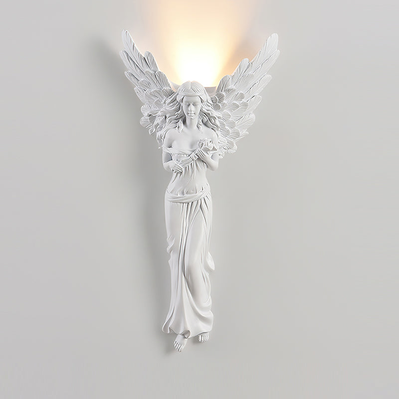 Standing-angel Clérachic wall light, lit, on a pale wall, a soft warm glow rising above its feathered wings.