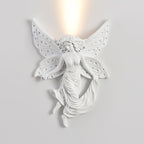 Fairy-shaped Clérachic wall light, lit, on a pale wall, with the glow passing up through the gap between its wings.