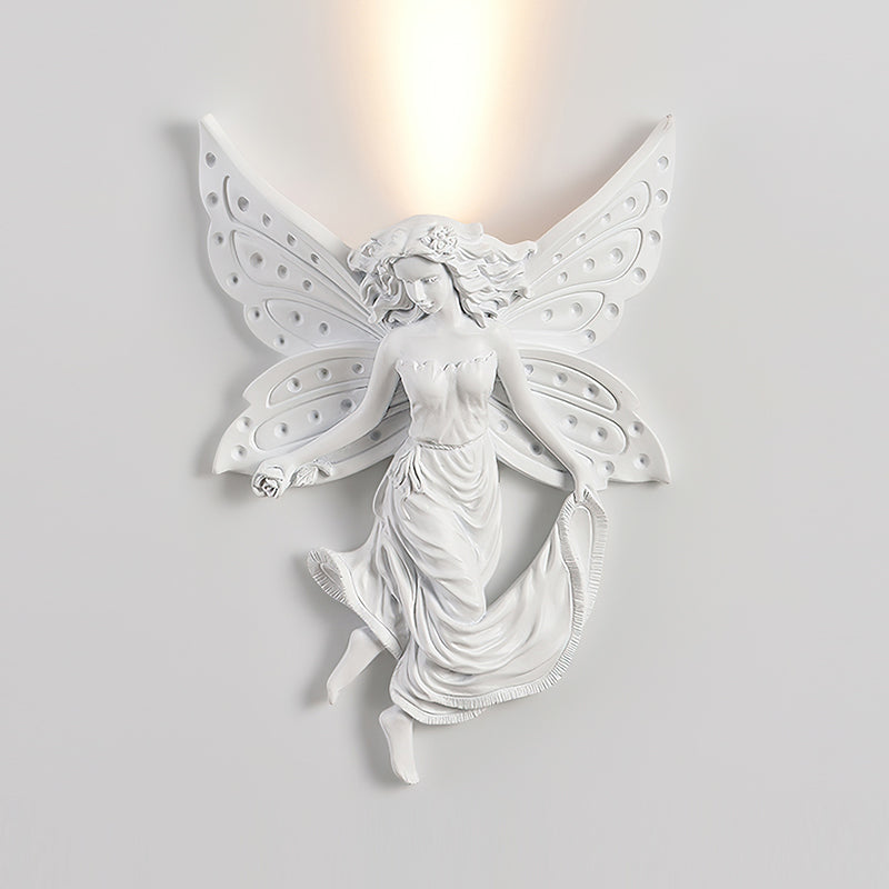 Fairy-shaped Clérachic wall light, lit, on a pale wall, with the glow passing up through the gap between its wings.