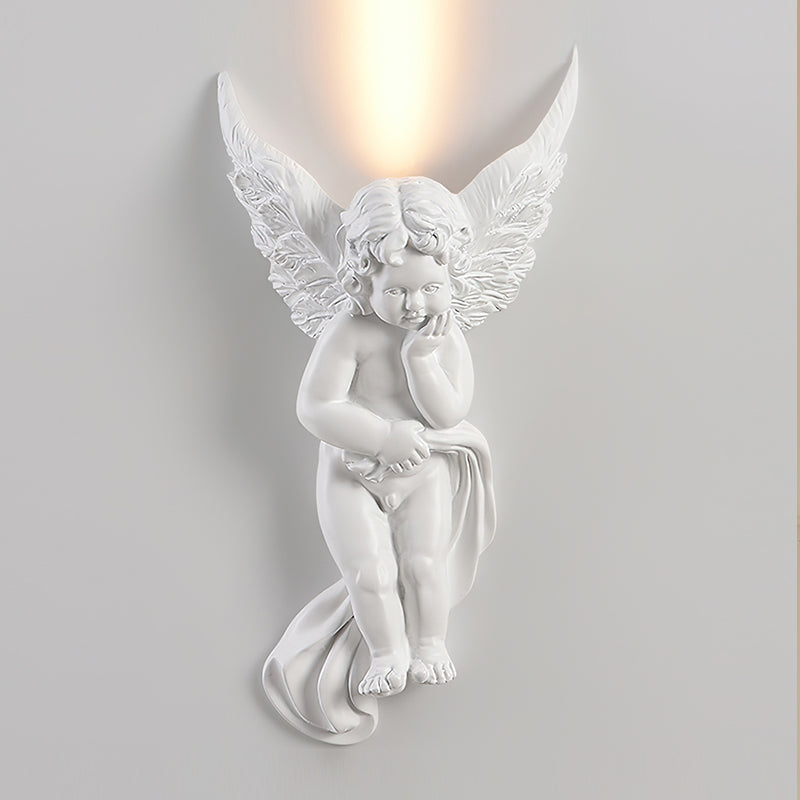 Cherub Clérachic wall light, lit, shown close on a pale wall, with a bright warm uplight above its wings.