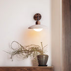 Lit Clérachic wall light above a console, its warm glow falling on a wall near a dried branch in a dark glazed pot.