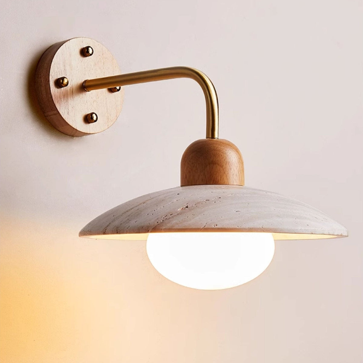 Close view of the travertine dome, wooden cap, brass-toned arm and lit bulb on this Clérachic wall light.
