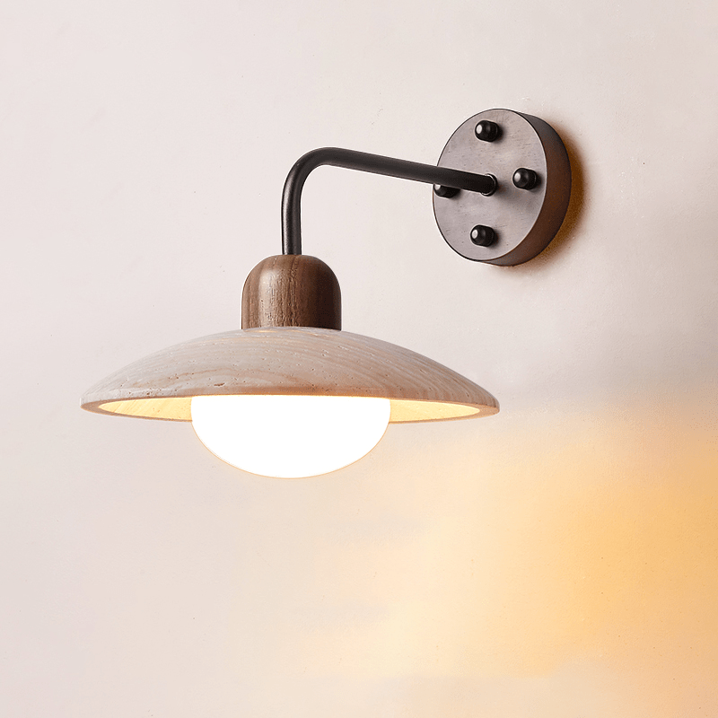 Clérachic wall light with a black arm and dark wooden plate, its travertine dome lit warmly from underneath.
