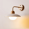 Clérachic wall light with a gold-toned arm and a pale wooden plate, the glass bulb glowing under the travertine dome.