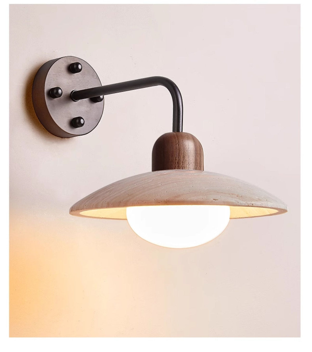 Clérachic wall light with a black arm and a dark round plate, shown lit against a soft peach wall.