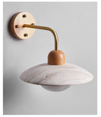 Clérachic wall light with a brass-toned arm on a grey backdrop, the travertine dome catching soft light above the bulb.