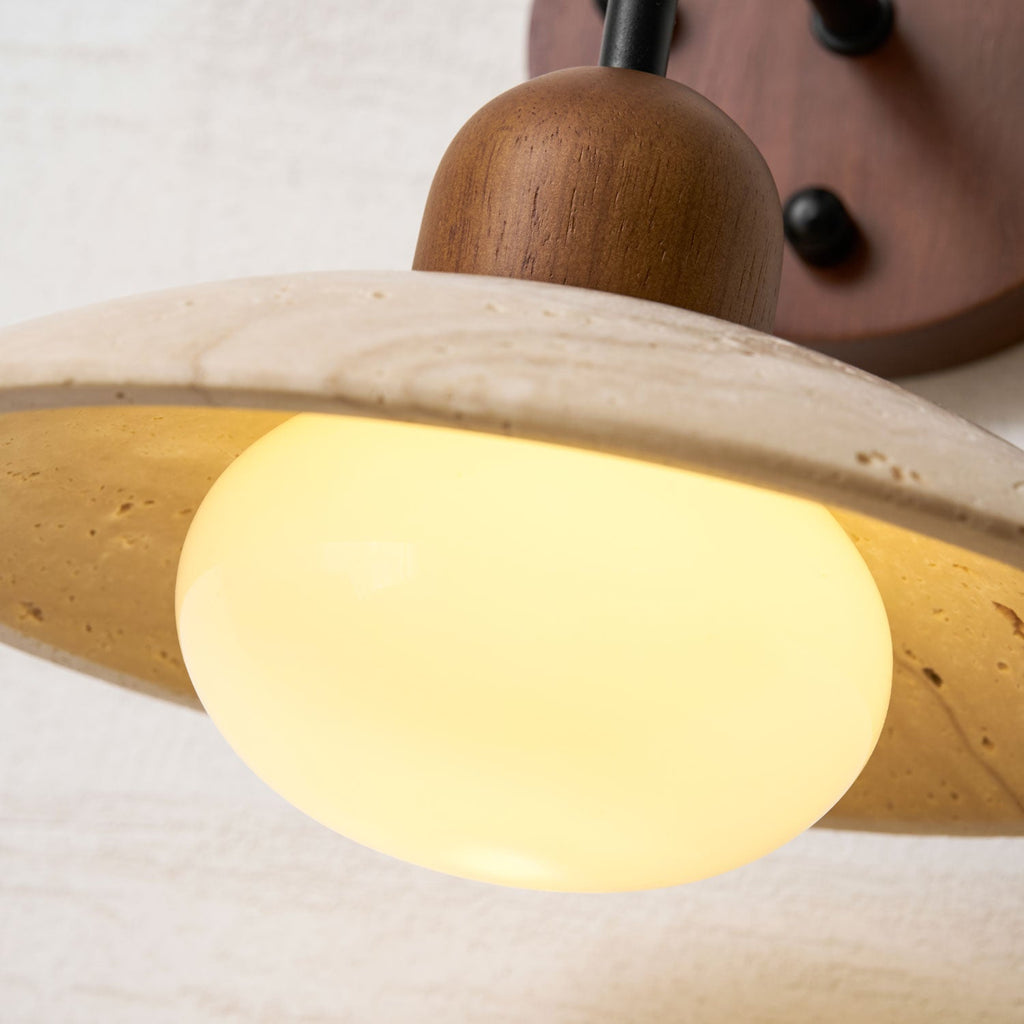 Close view of the lit opal bulb under the pitted travertine dome of this Clérachic wall light.