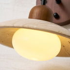 Close view of the lit opal bulb under the pitted travertine dome of this Clérachic wall light.