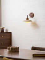 Clérachic wall light glowing in the upper half of a textured wall, with a walnut dresser and a stone dish below.
