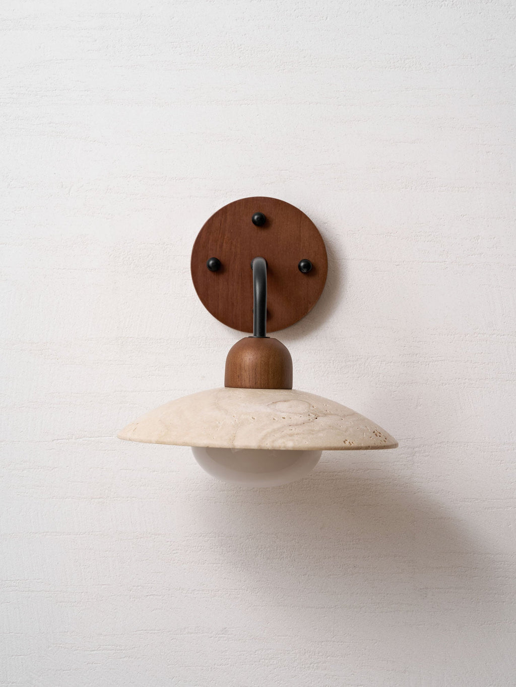 Straight-on view of this Clérachic wall light, its arm hidden behind the cap above the travertine dome and glass bulb.