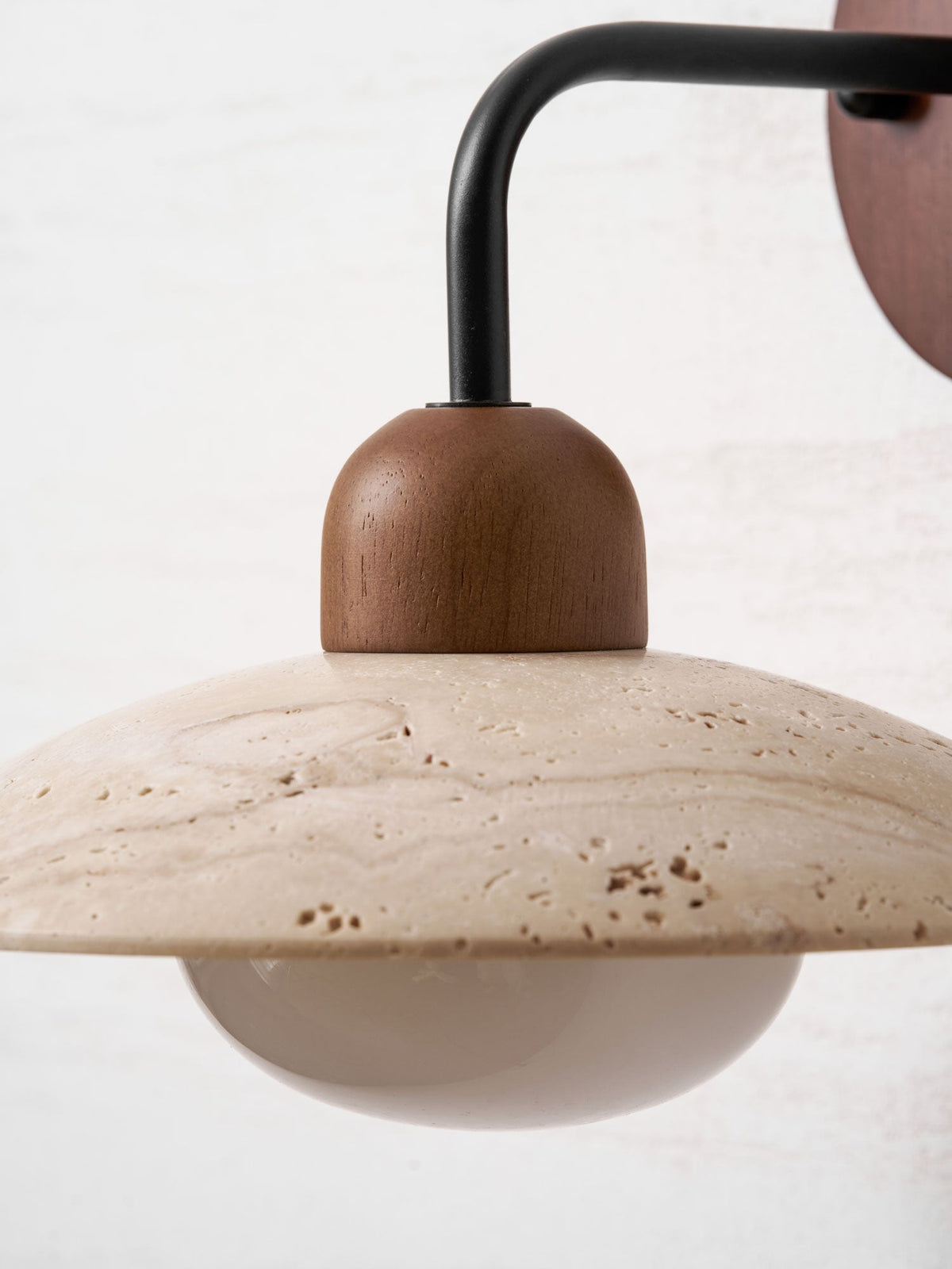 Close view of the walnut cap, black arm and veined travertine dome on this Clérachic wall light.