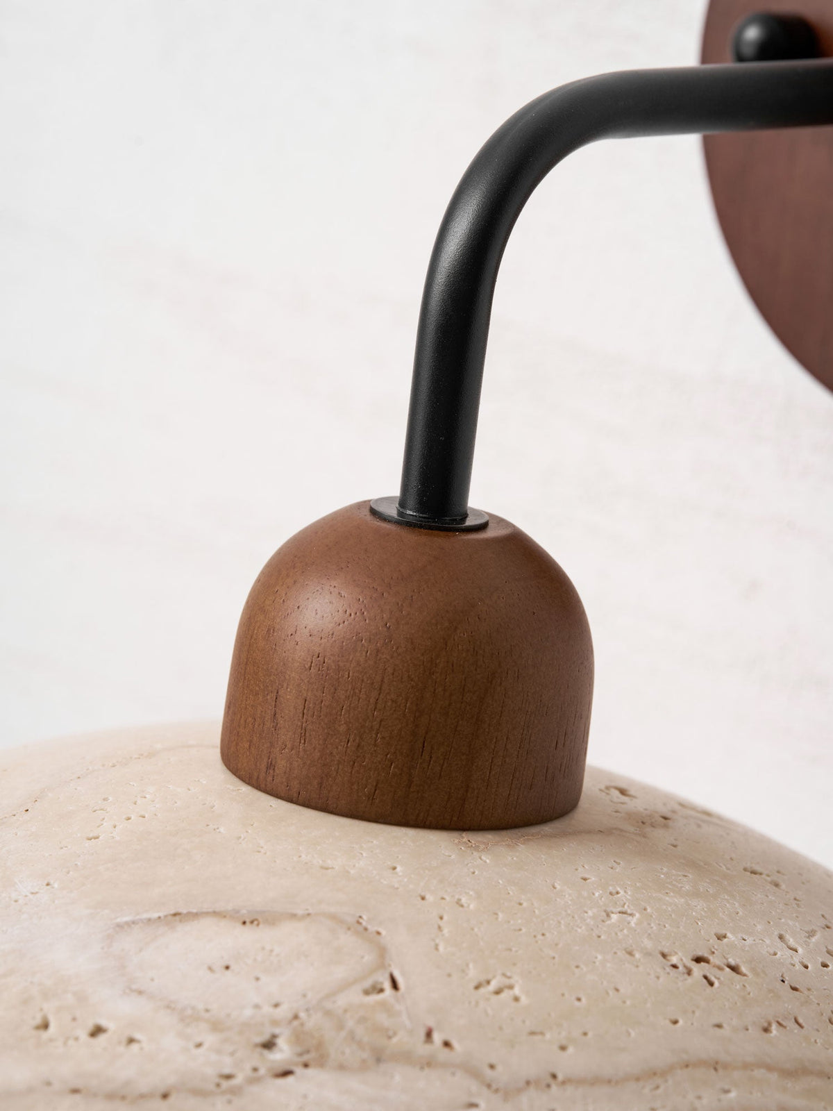 Close view of the black arm meeting the walnut cap on this Clérachic wall light, with the travertine dome below.