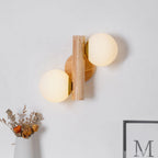 This Clérachic wood sconce on a pale wall, its two frosted globes above a vase of dried flowers and a framed print.