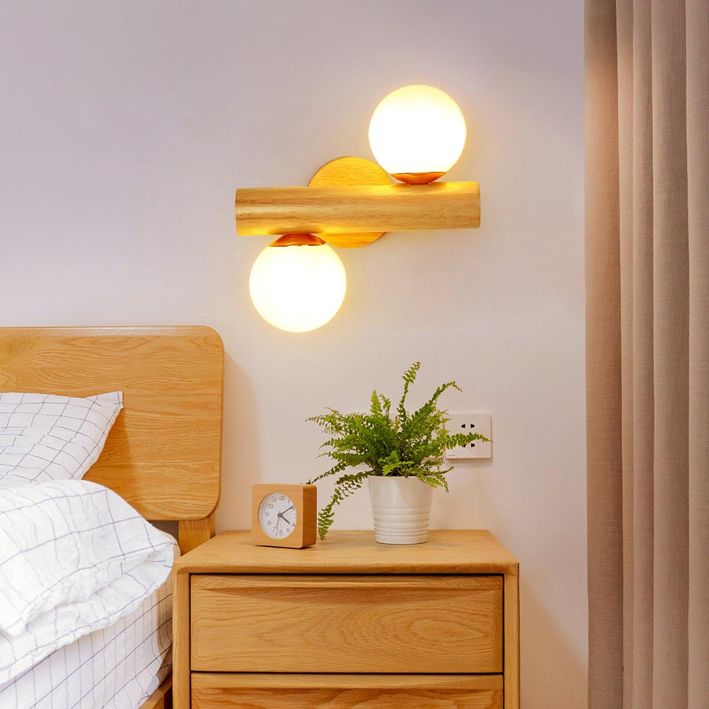 Clérachic wall sconce turned sideways above a bedside table, its two globes glowing beside a wooden headboard and a small clock.