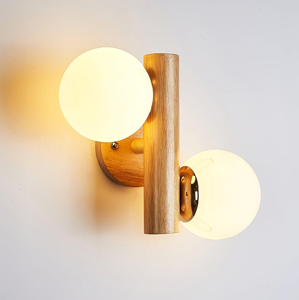Lit Clérachic wood wall light with two opal globes, the warm glow spreading across a pale wall behind the wooden rod.