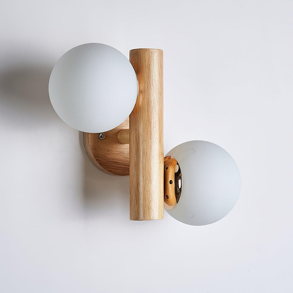 Unlit Clérachic wall sconce in profile, two frosted white globes on a round wooden backplate against a light grey wall.