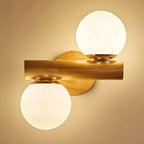 Close view of the horizontal wooden rod on this Clérachic sconce, the two lit globes filling a warm amber-toned wall with light.