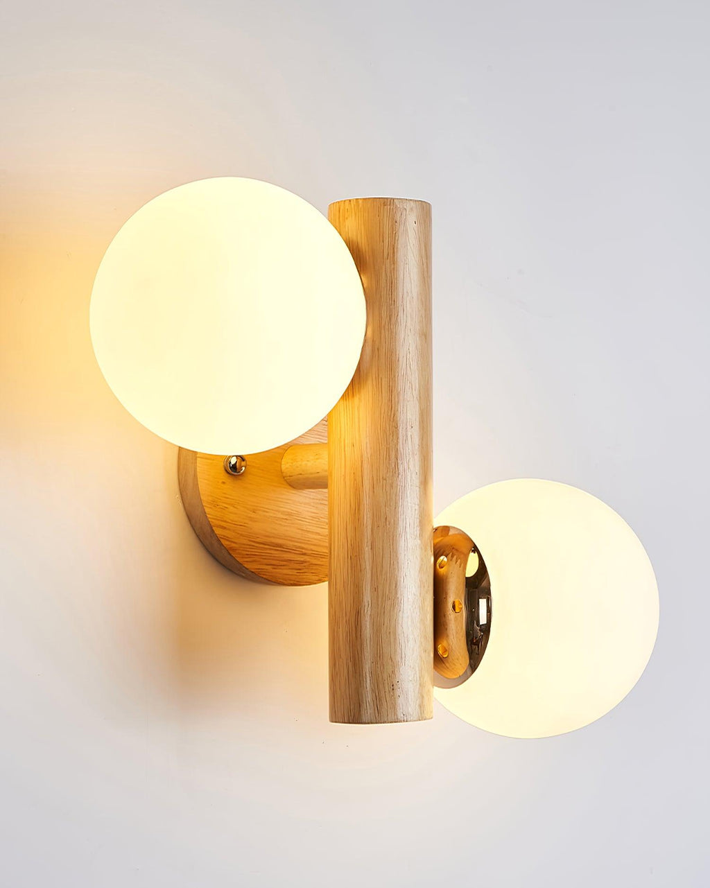 Lit Clérachic wall sconce with its upright wooden rod, a golden glow around the globes on a soft grey wall.