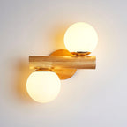 This Clérachic sconce lit in the evening, its horizontal wooden rod between two bright globes on a grey wall.