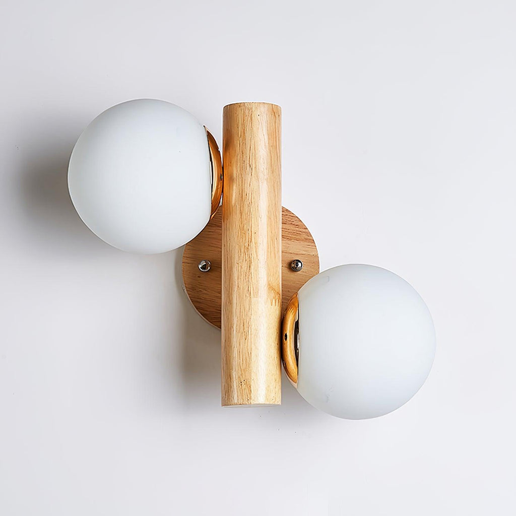 Unlit Clérachic wall sconce from the front, two matt white globes and a wooden rod on a plain pale wall with a soft shadow.