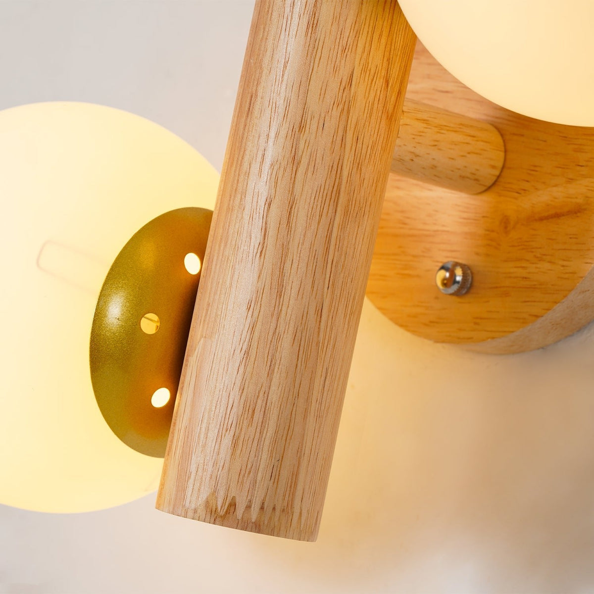 Close view of the gold-toned cap and screw holes behind a glowing globe on this Clérachic wood sconce.