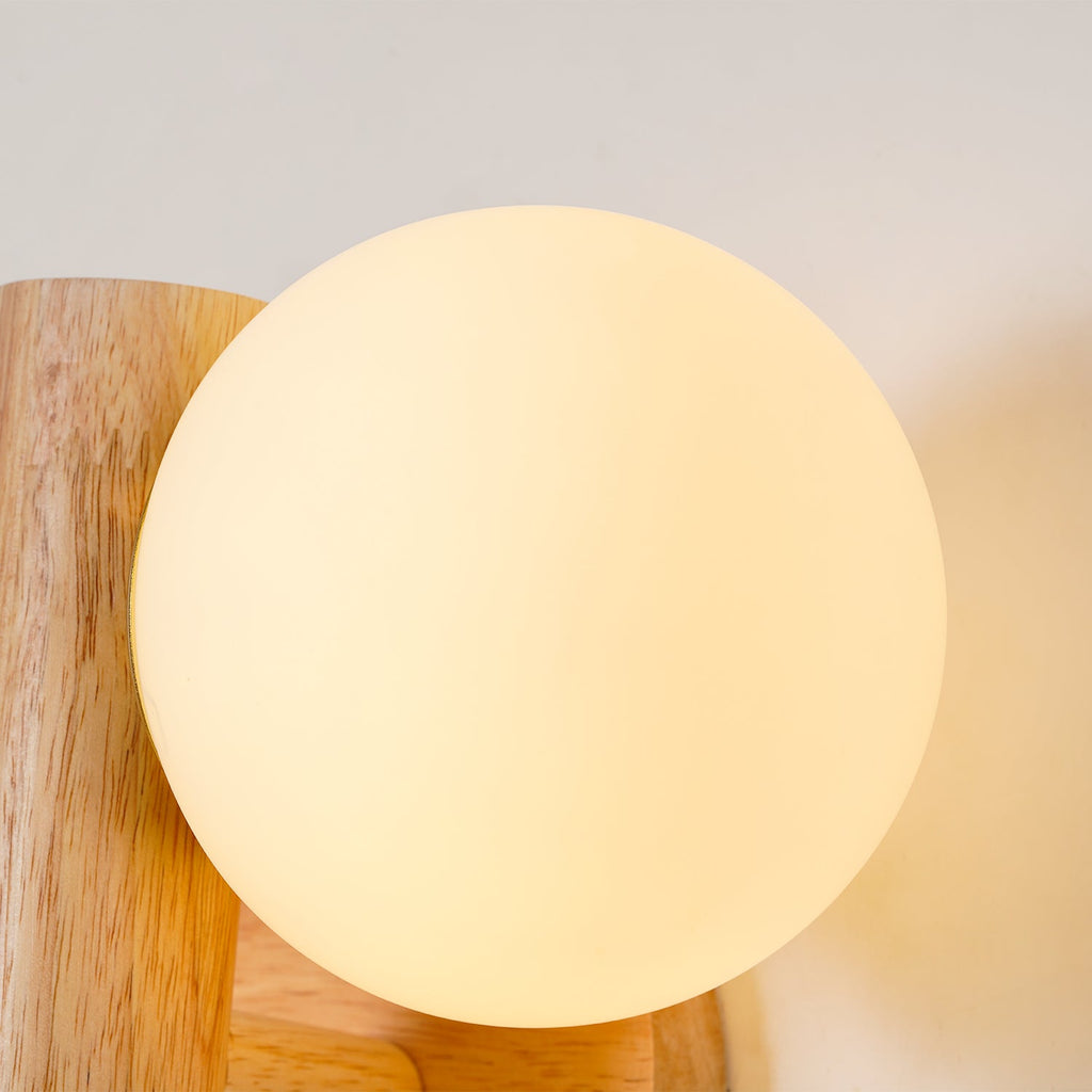 Close view of a lit frosted glass globe on this Clérachic wall sconce, its warm light visible against the wooden rod.