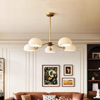 A Clérachic chandelier with five white shades hangs in a panelled living room above a tan leather sofa and framed prints.