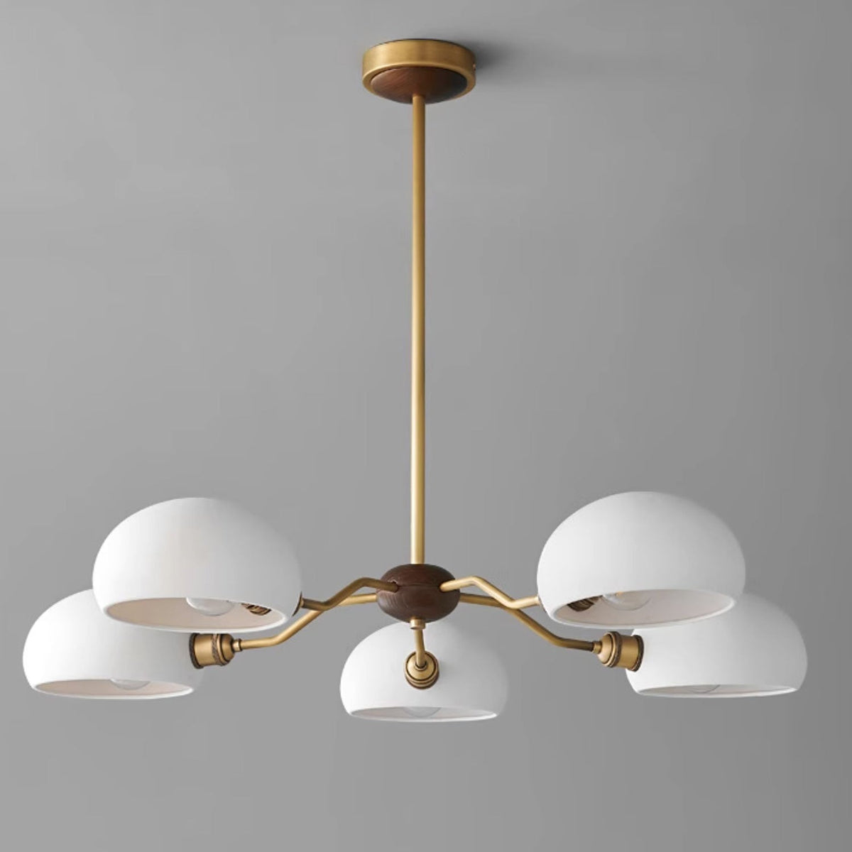 Five white ceramic shades on brass arms, a Clérachic chandelier with a walnut and brass canopy against a cool grey wall.