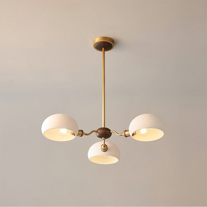 Slightly angled view of the three-light Clérachic chandelier, with its white shades, brass arms and walnut hub.