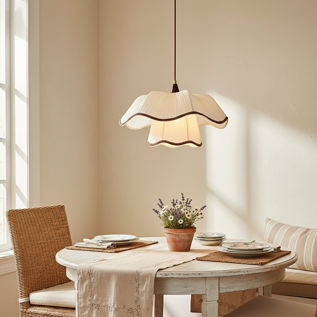 Pleated scalloped shade of a Clérachic pendant hanging above a round white dining table with a terracotta pot of lavender, in soft window light.