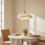 Pleated scalloped shade of a Clérachic pendant hanging above a round white dining table with a terracotta pot of lavender, in soft window light.