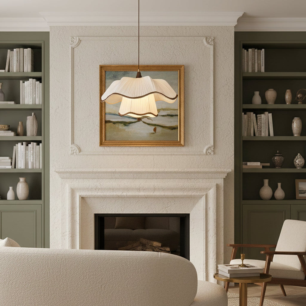 Ruffled white shade of a Clérachic pendant glowing in front of a framed landscape painting, between green bookshelves and a plaster fireplace.